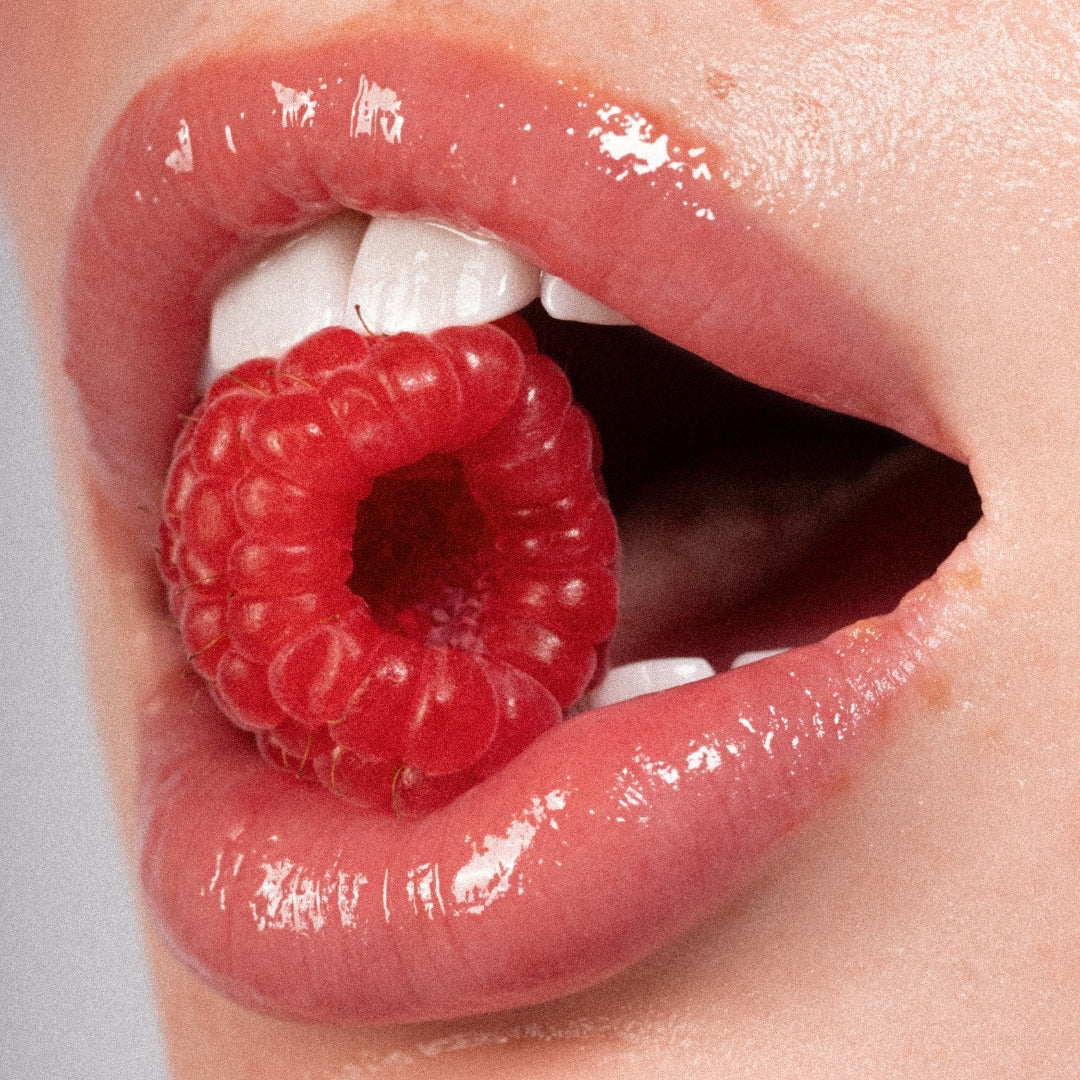 Close-up of a mouth with an-gloss on lips with a raspberry inside
